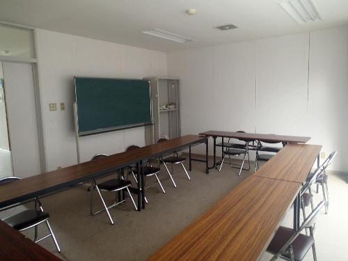 カーペット敷きの研修室。2人掛けの机や黒板があります