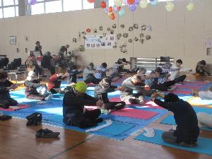 写真：体育館の床に座り、コツコツ貯筋体操の体験をする地域住民