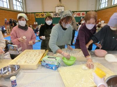 写真：炊きたての新米でおにぎりを作る参加者。テーブルの上には出来上がったおにぎりがたくさん並んでいます。