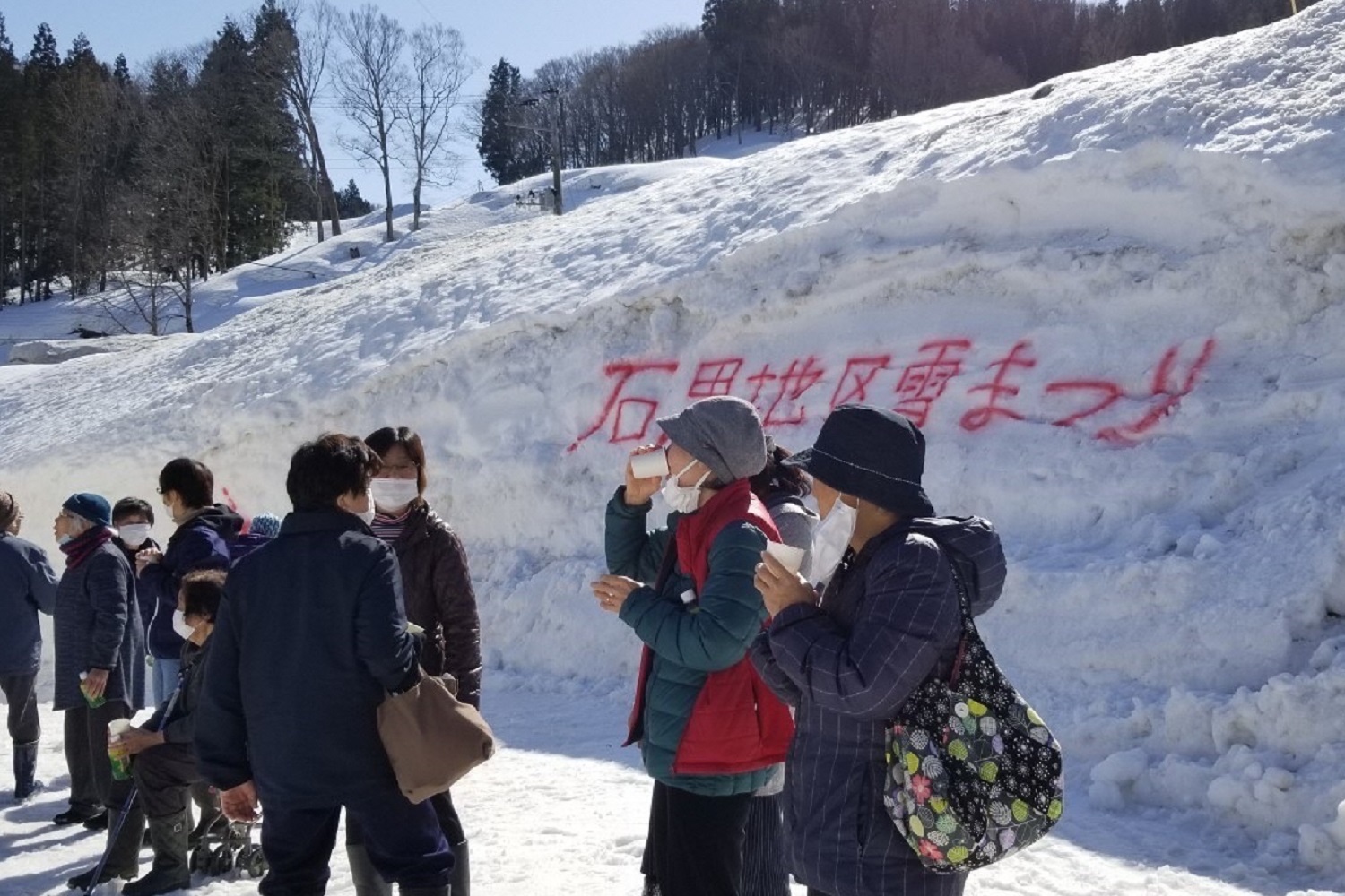 写真：雪祭りイベントに訪れた参加者の皆さん。後ろには人の背丈以上の雪が積もっています。
