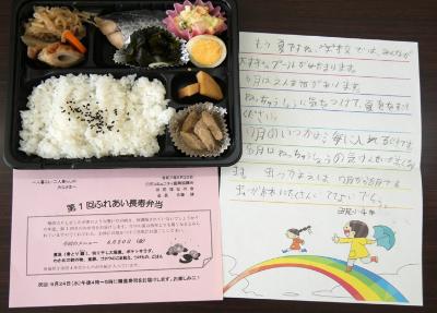 写真：ご飯と煮物、マカロニサラダ、焼き魚が入ったある日のお弁当。小学生が書いた手紙も並べられています。