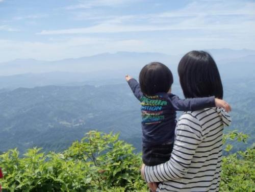 女の人に抱き上げられた子どもが遠くに見える山を指でさしており、空と山が青くてきれいな写真