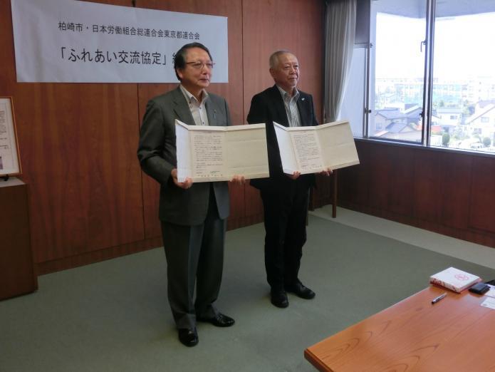市長と岡田会長がそれぞれに協定書を広げて持ち、並んで立っている写真