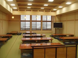 机が並び、窓の向こうには日本海が広がっている食事もできる大広間の写真