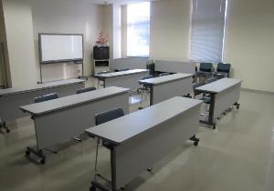 机と椅子がきれいに並べられ、ホワイトボードとテレビも完備された会議室の写真