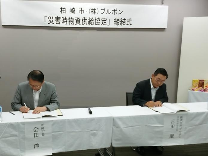 市長と株式会社ブルボン吉田社長が協定書にサインをしている様子の写真