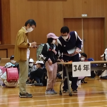 写真：小学校体育館での引き渡し訓練の様子。教職員が児童に迎えに来た保護者の確認をしています