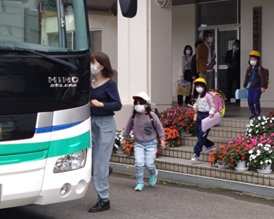 写真：小学校の玄関に横付けされた避難用のバスに乗り込む児童たち