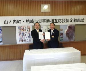 応援協定調印後、書類を持ち笑顔で握手を交わす竹節山ノ内町長と会田市長の写真