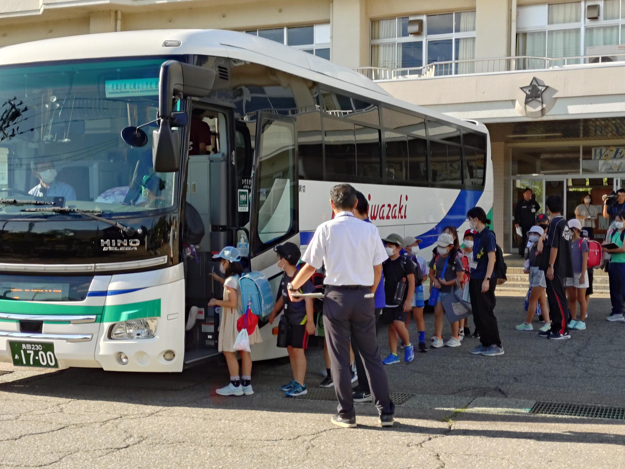 写真：学校の玄関前に停車したバスに児童が乗り込んでいます
