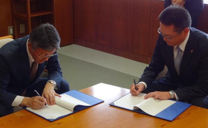男性二人が、それぞれが並んで協定書にサインをしている様子の写真