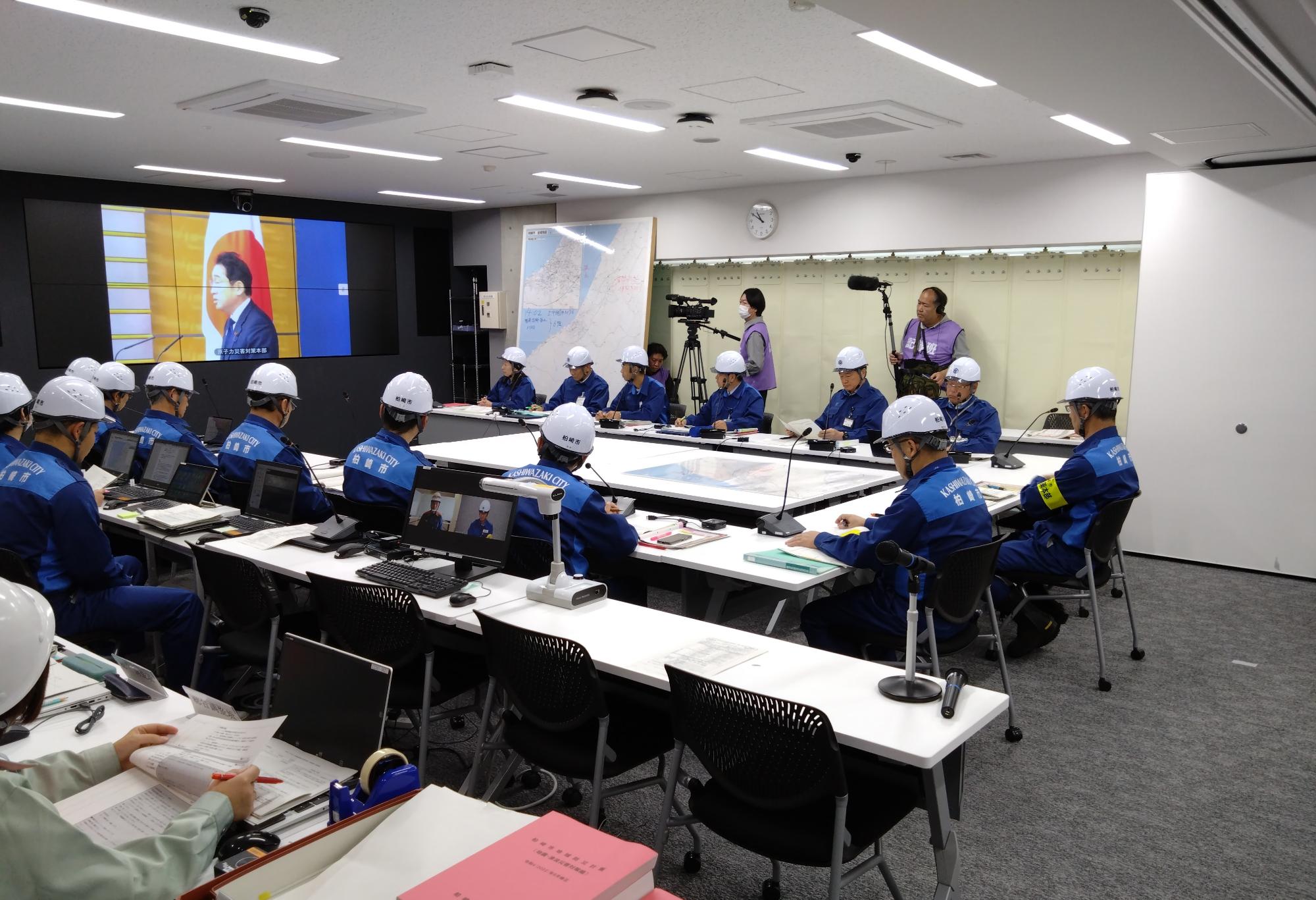 写真：市役所の防災対策室で訓練関係者らとテレビ会議を行っている様子