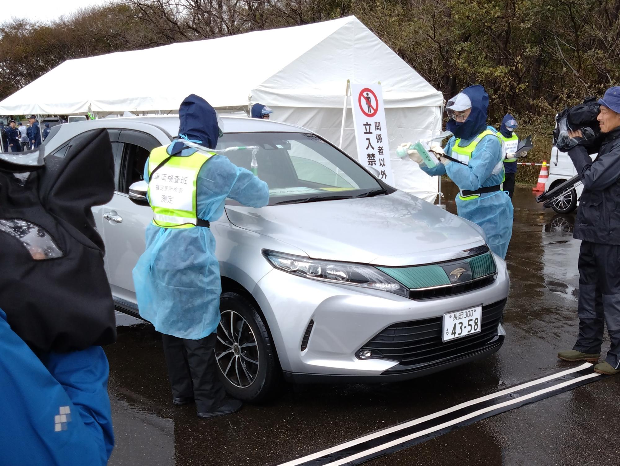 写真：避難してきた車両の放射線スクリーニングを行う職員。車体に機械をかざして、放射能物質が付着していないかどうかを調べています。