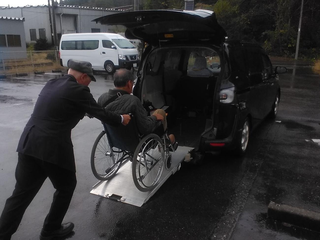 写真：スロープ付きの軽自動車に、車椅子に乗ったままの男性を乗車させる様子