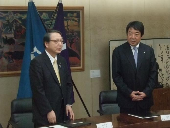 協定締結後机から立ち上がり、山本前橋市長の横に立ちあいさつをする会田市長の様子の写真