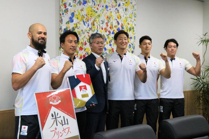 市長が水球日本代表男子チームの監督、主将、選手と並んでガッツポーズで記念撮影している様子