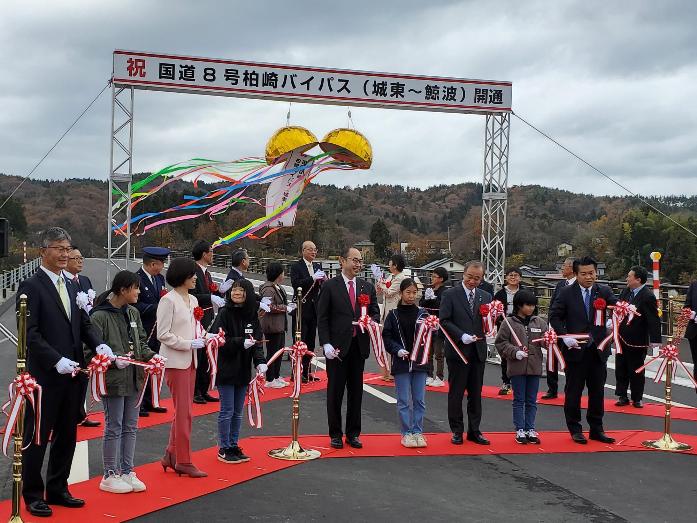 開通する国道8号柏崎バイパスの道路上で、市長が国会議員や新潟県議員、子どもたちとテープカットしている様子