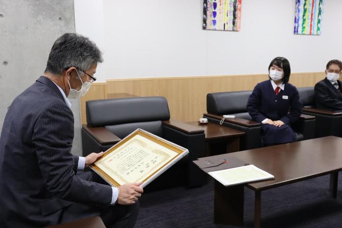 写真：市長が品田さんが受賞した作文コンクール優秀賞の表彰状を座りながら見ている様子