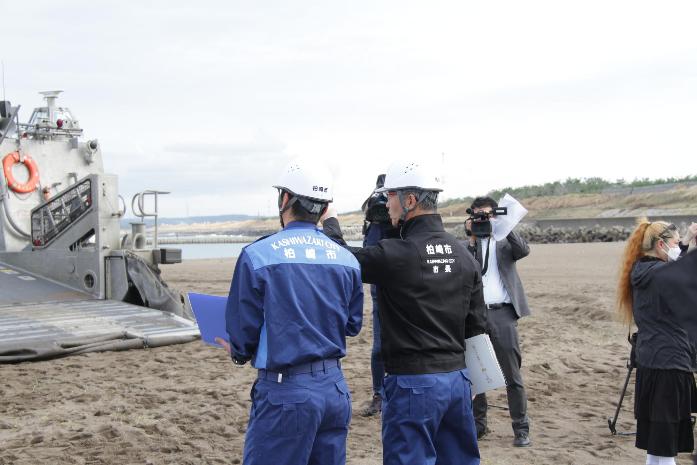 防災服を着た市長が柏崎中央海水浴場で船舶避難訓練を見学している様子