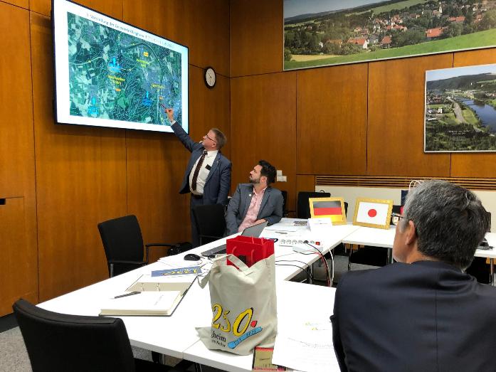 市長がドイツにあるオーブリヒハイム自治体から画面に映し出された資料を使って説明を受けている様子