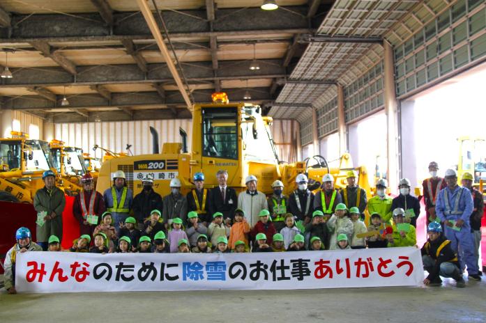 市長が除雪事業者と東部保育園の園児と一緒に除雪車の前に並んで記念撮影している様子