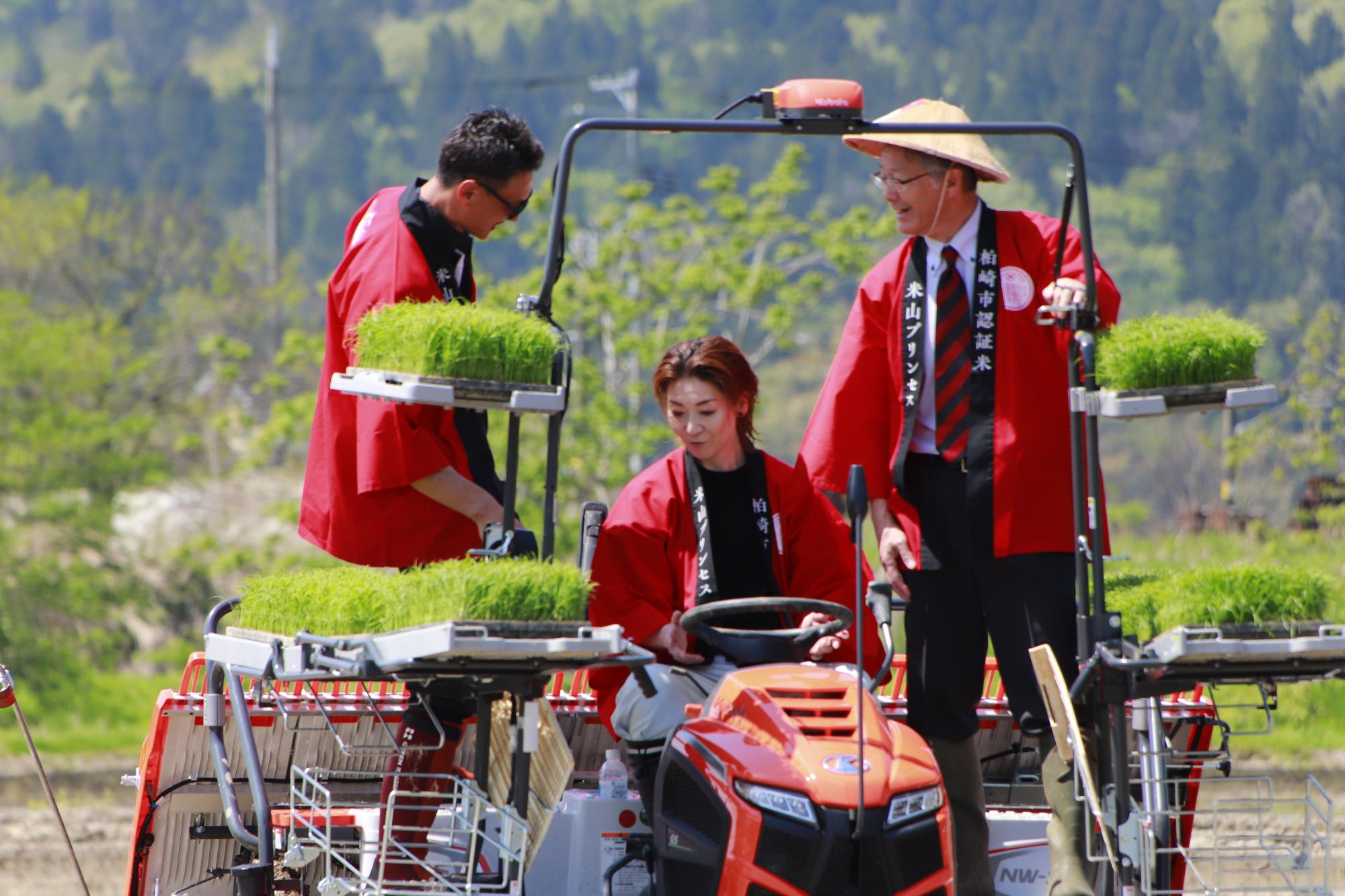 写真：越乃リュウさんが操縦する田植え機に同乗する櫻井市長