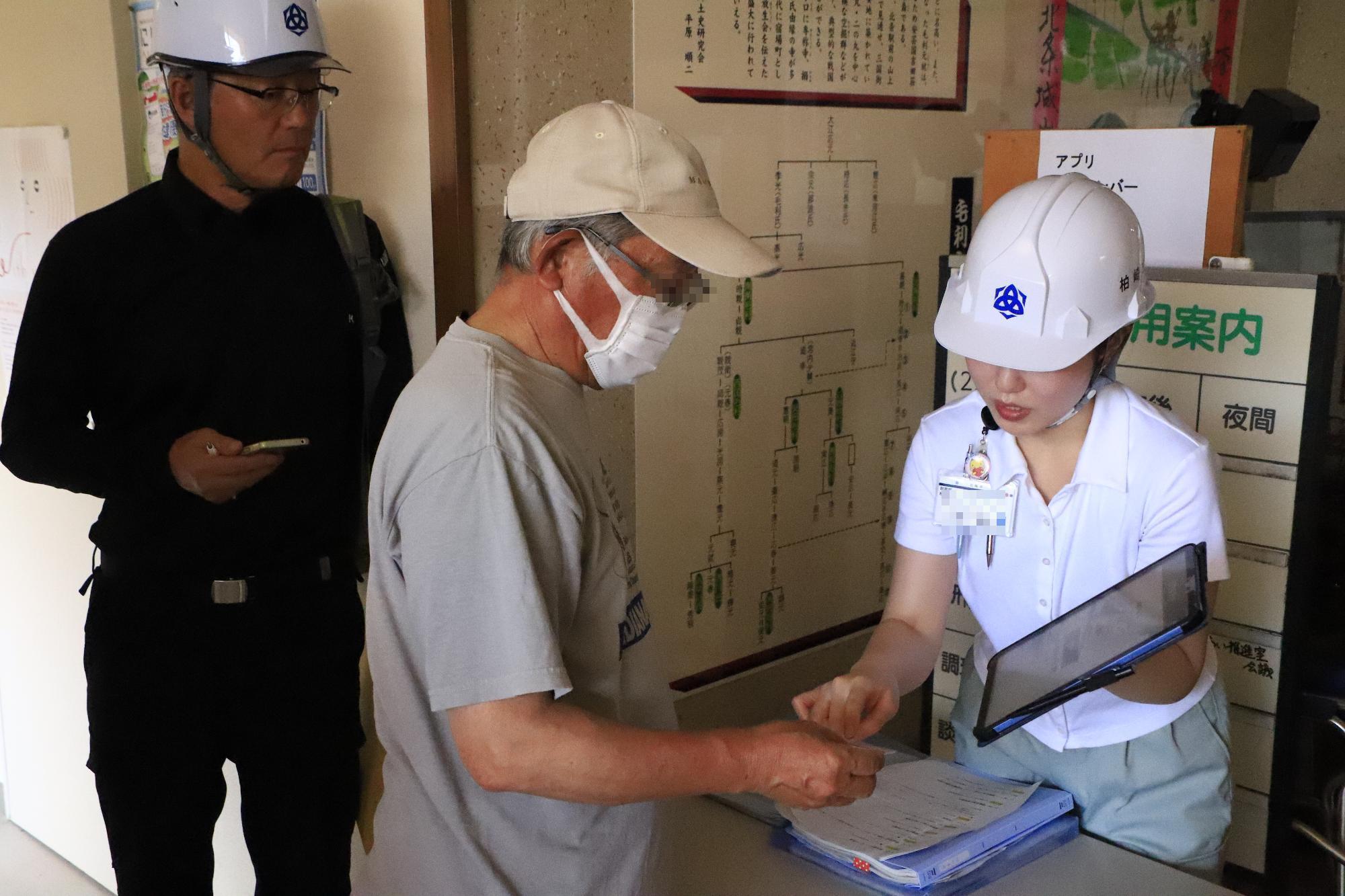 写真：住民避難訓練で模擬マイナンバーカードを提示する市民と確認する市職員。その後ろに視察中の櫻井市長がいます