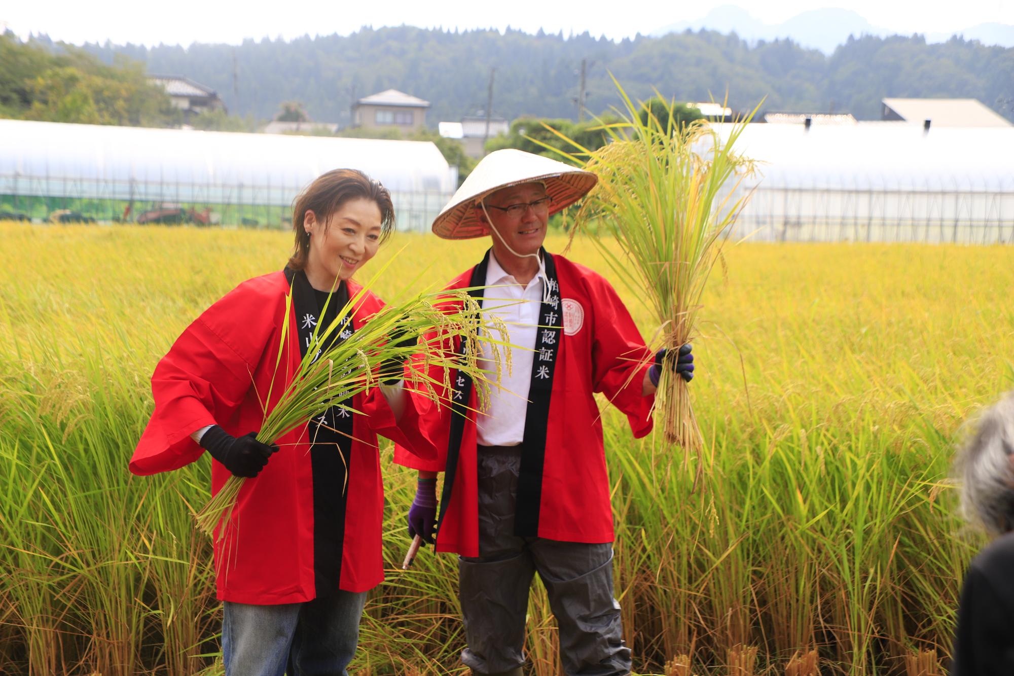 写真：黄金色に実った稲の束を持ち、笑顔を浮かべる市長と越乃リュウさん