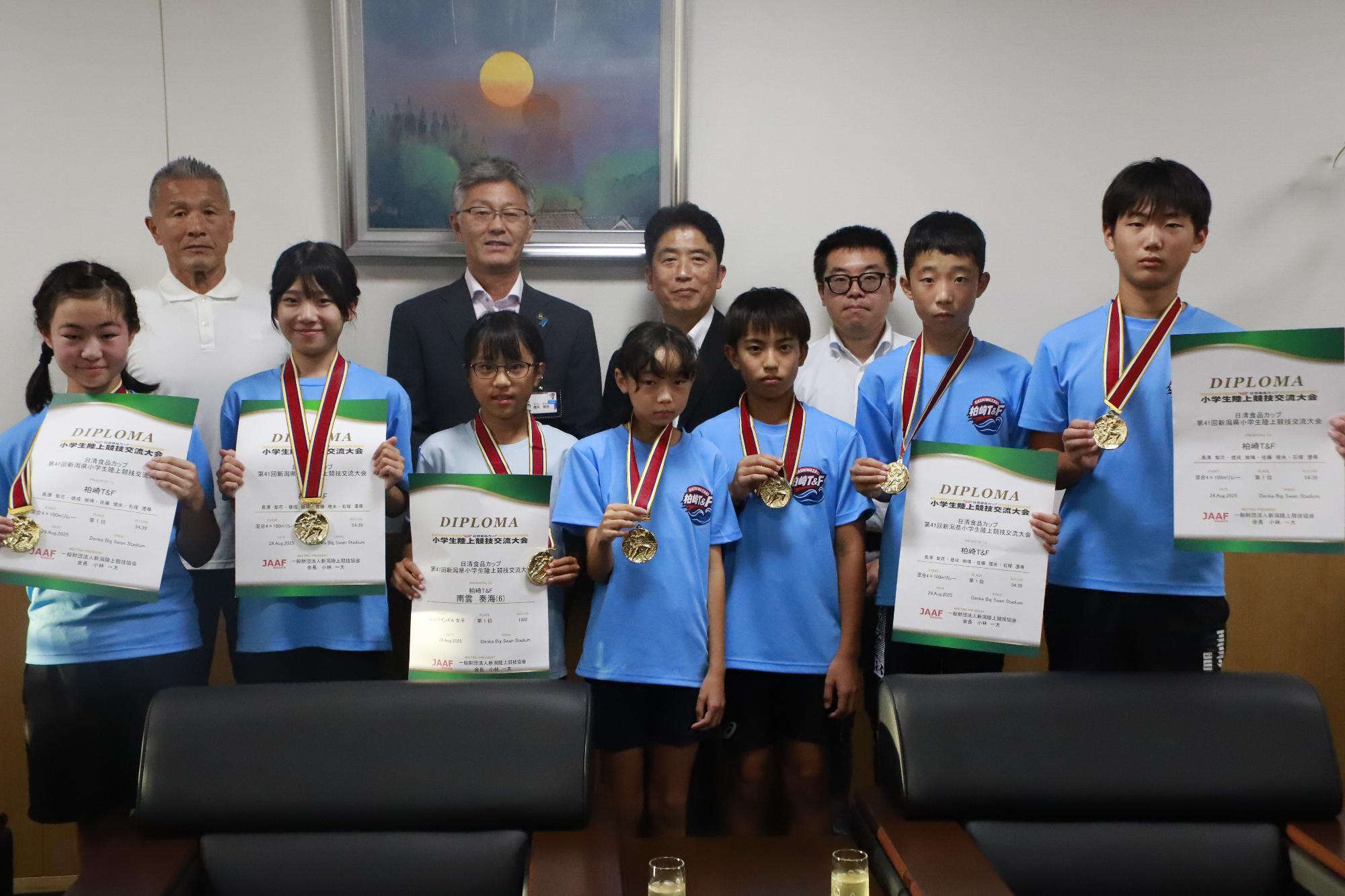 写真：前列に全国大会出場の報告に訪れた小学生7人がメダルや賞状を持ち並んでいます。後列中央に市長が、その両脇にクラブの指導者が並んでいます