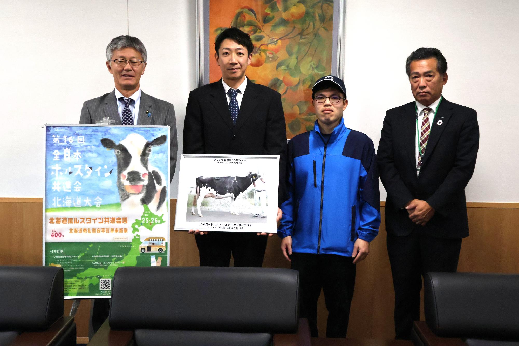 写真：市長と大会出場者3人が並んでいます。品評会のポスターと出品する乳牛の写真を持っています。