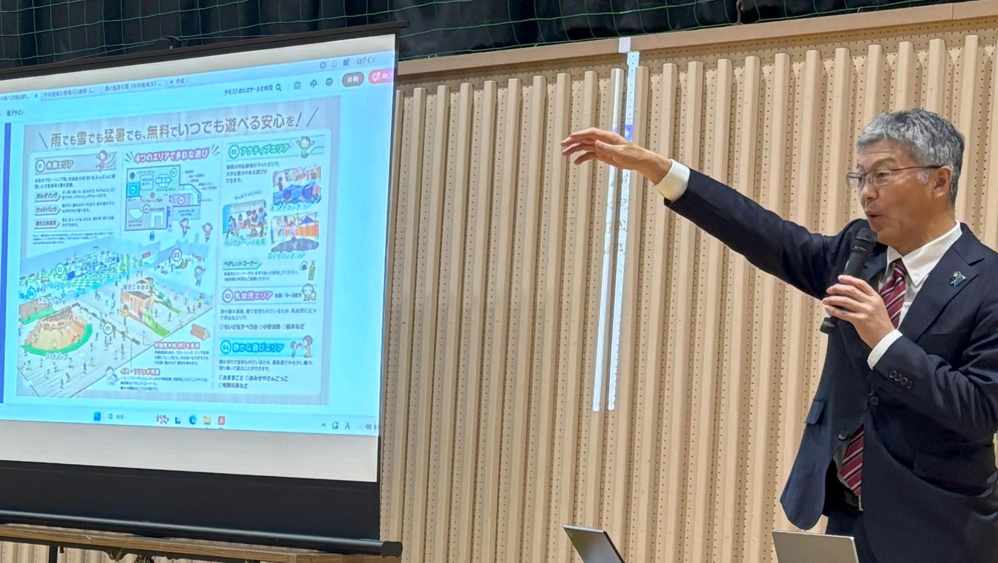 写真：資料を投影しながら、マイクを持ち住民の皆さんに施策を説明する市長