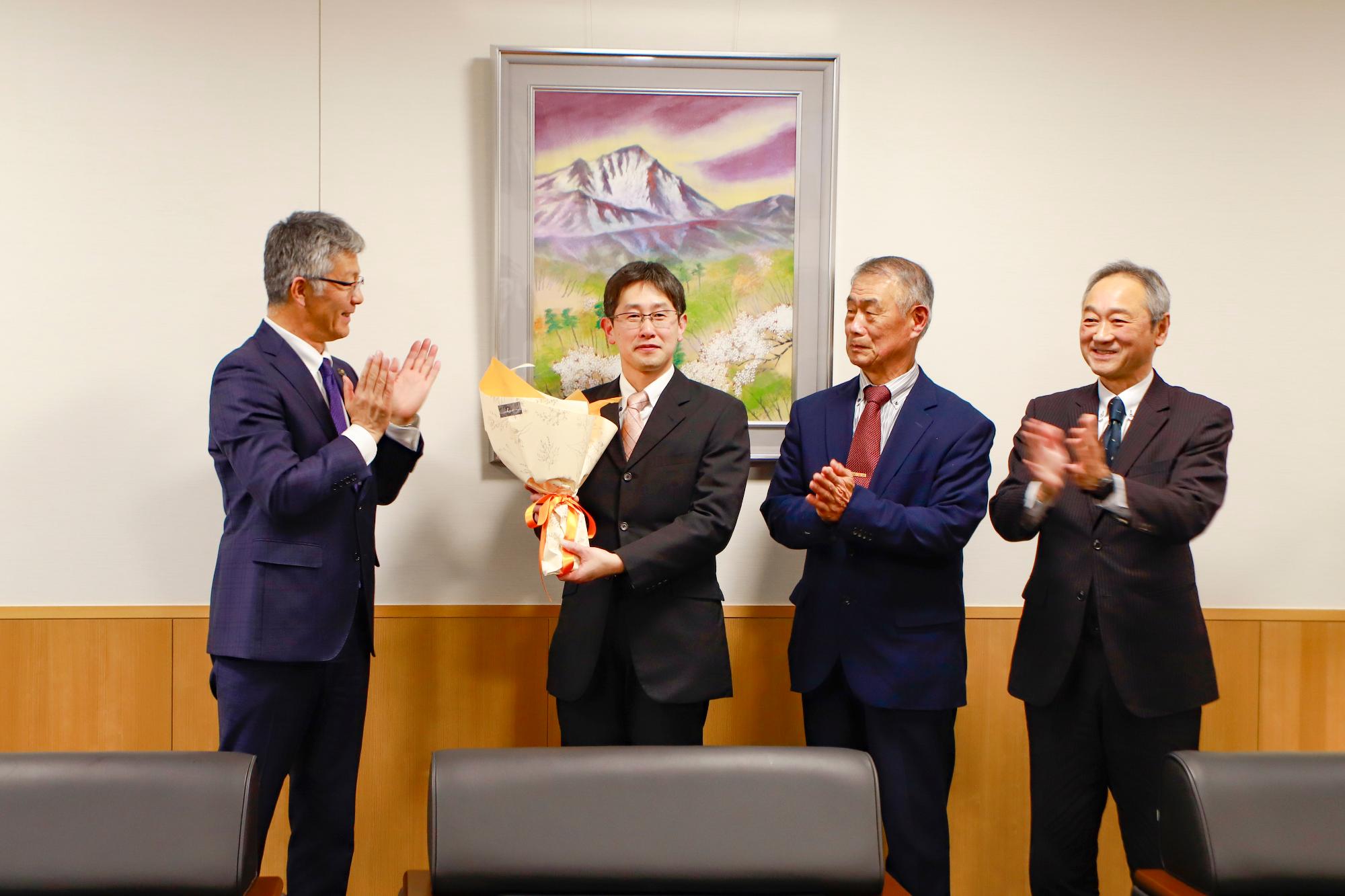写真：市長が花束を持った酒井隊員に向け、地域の方とともに拍手を送っています