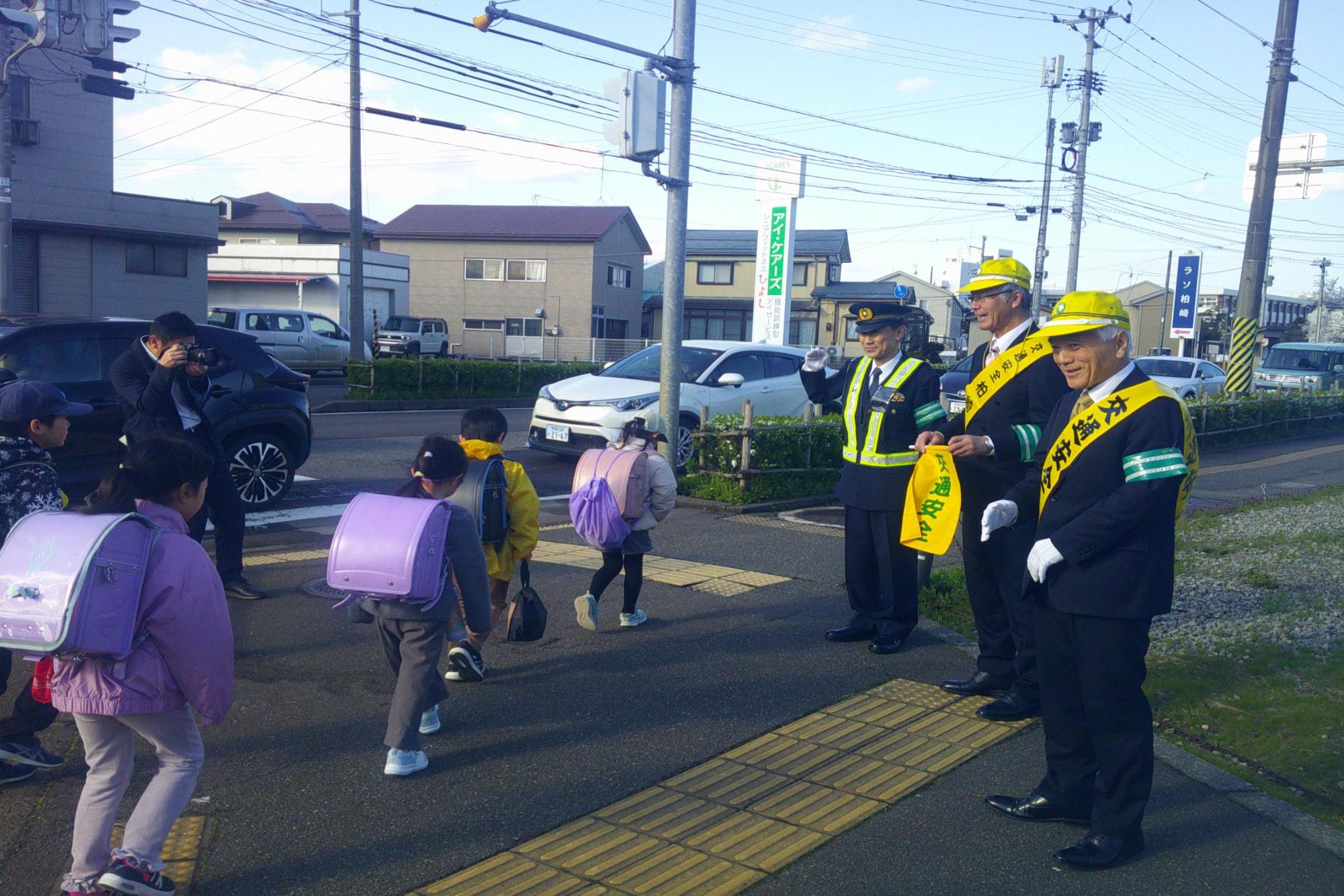 写真：黄色い帽子をかぶり、・黄色のたすきを身に付け、登校する児童たちに交通安全を呼び掛ける市長たち