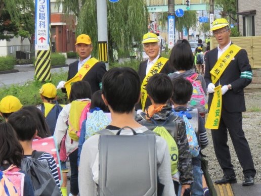 黄色い帽子とたすきをかけた市長らが登校中の小学生らに声をかけている様子