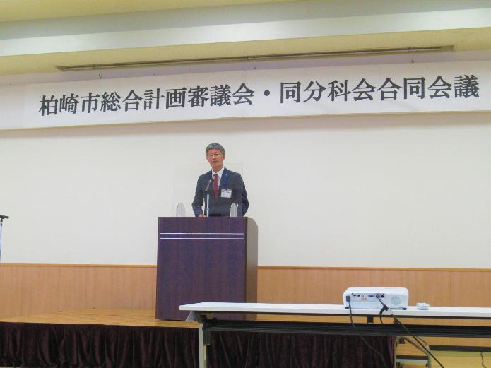 市長が、柏崎市総合計画審議会・同分科会合同会議と記された横看板の下にて、ステージ上中央の演台で話をしている写真