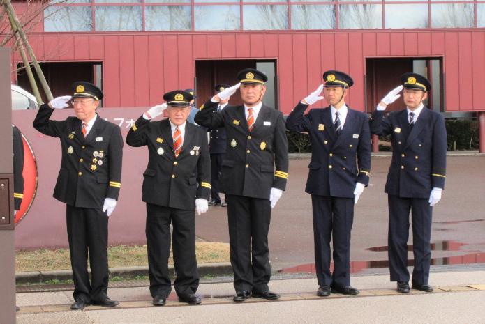 消防団の制服を着て、白い手袋を両手にはめ、右手で挙手をしている副市長ら5人の男性