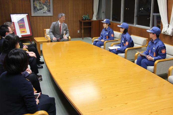 青い制服を着て帽子をかぶった学生消防団員3人が、市長応接室で市長と懇談している写真