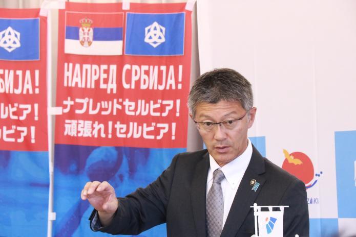 セルビアを応援するのぼり旗の前で、発表する櫻井市長の様子