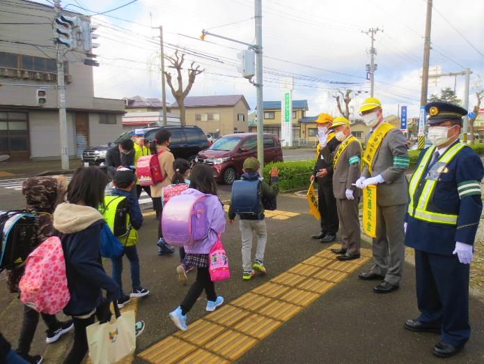 日吉町交差点で、黄色い帽子とたすきを身に付けた市長が関係者の方と、登校する児童へ声を掛けている写真