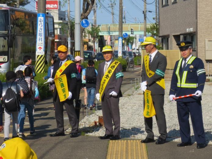 交通安全を促す黄色いたすきと旗を持ち、小学生の通学を見守る市長らの写真