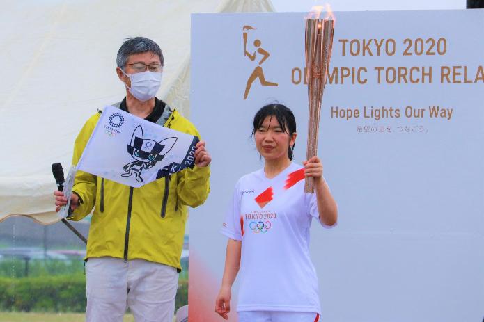 駅前公園の仮設ステージの上で、聖火を持った女性のランナーと東京オリンピックの旗を持つ市長の写真