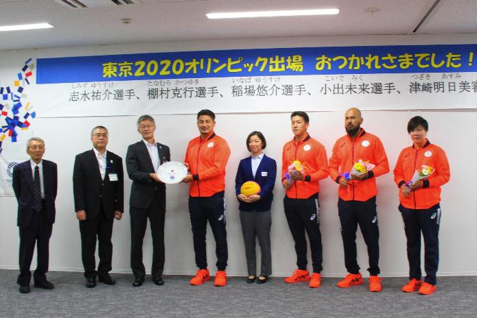 赤いジャージを身につけた東京オリンピック水球市内関係出場選手と市長と教育長と西川理事長が横に並んでいる写真