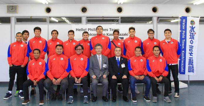 赤いおそろいのジャージを着たフィリピンの水球男子代表チームがにこやかに市長・教育長と集合写真をとっている様子