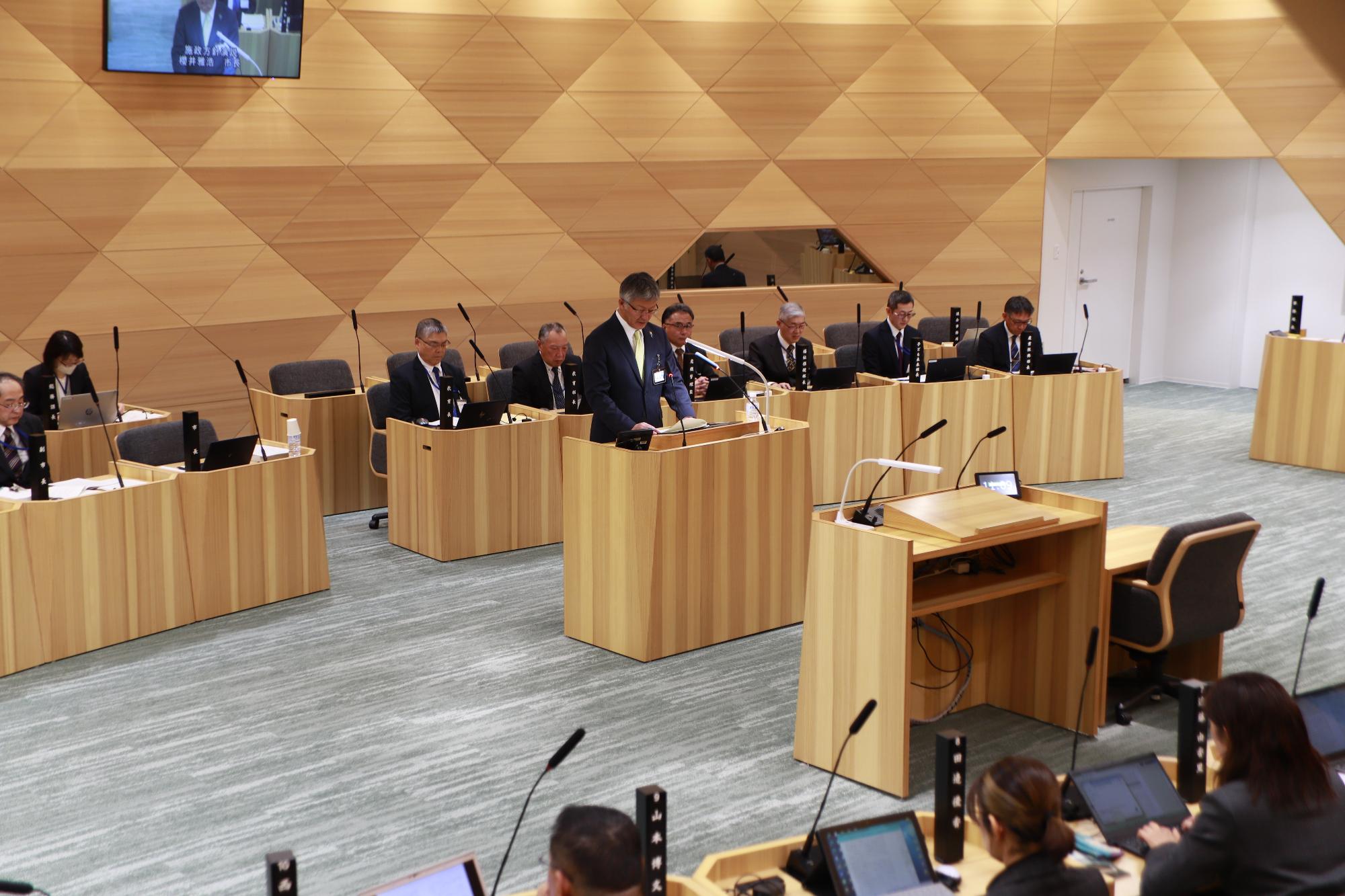 写真：施政方針演説会場の柏崎市議会議場。議場の中ほどに演台があり、その後ろには市幹部職員の席があります。向かいに議員席があり、奥中央には議長席と副議長席があります。