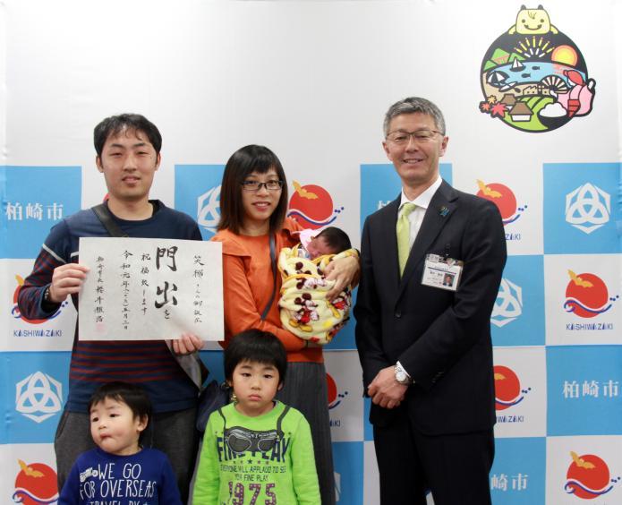 門出を祝福するメッセージを手にする出生届を出しに来られた家族と市長の写真