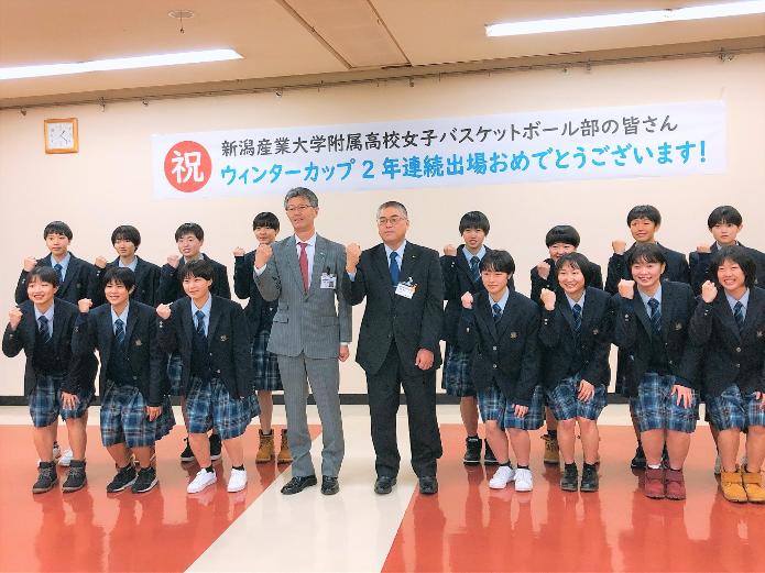右腕でガッツポーズを作る市長、教育長、新潟産業大学附属高校女子バスケットボール部15名の選手が、2列で並んでいる写真
