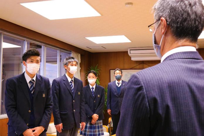 カメラに背を向けて立つ市長と、市長の方を見て話を聞いている3名の新潟産業大学附属高等学校陸上部選手