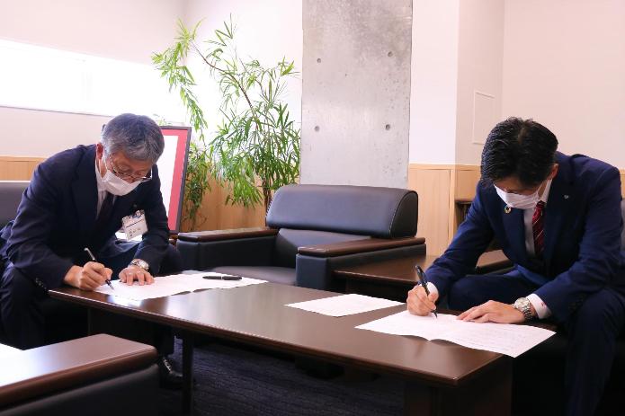 市長応接室で、調印所に署名中の市長と青年会議所理事長の写真