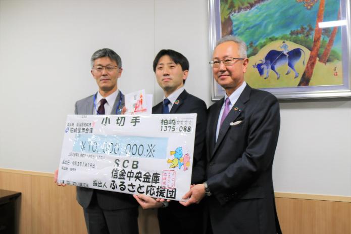 寄付いただいた目録に、市長と信金中央金庫の山田所長と柏崎信用金庫の小出理事長が手を添えている写真