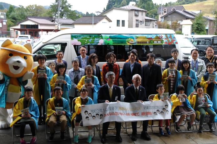 高柳みんなのバス新車両の前で、市長と高柳小学校の児童が横断幕を持って並んでいる写真